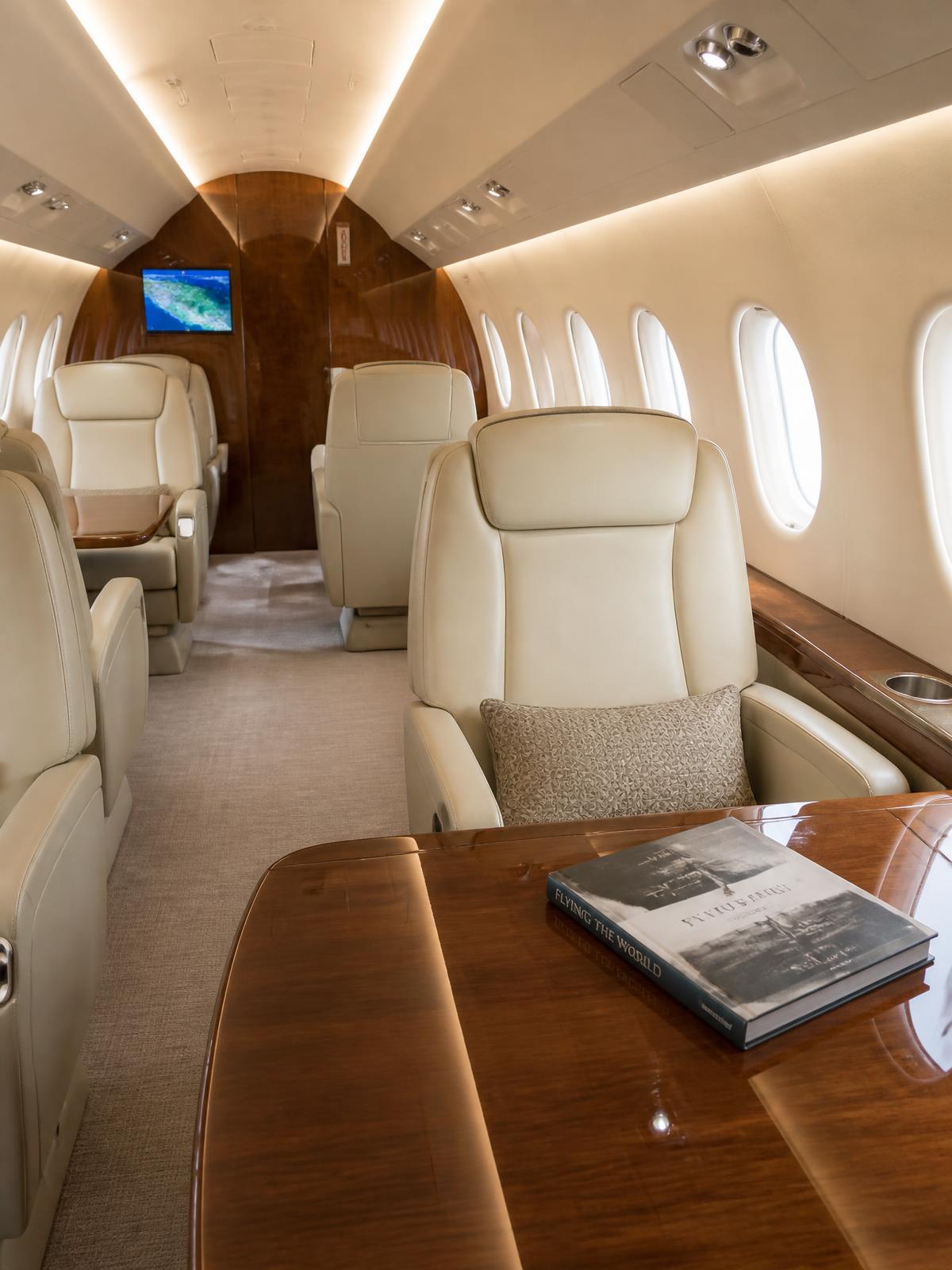 Private jet cabin with cream leather club seats and walnut tables